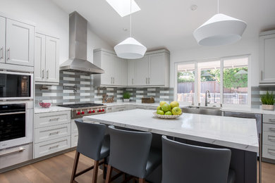 Example of a mid-sized minimalist l-shaped medium tone wood floor and brown floor eat-in kitchen design in San Francisco with a farmhouse sink, shaker cabinets, gray cabinets, granite countertops, gray backsplash, glass tile backsplash, stainless steel appliances, an island and white countertops
