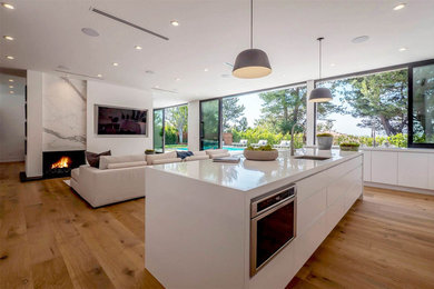 Large contemporary l-shaped open plan kitchen in Los Angeles with a submerged sink, flat-panel cabinets, white cabinets, composite countertops, stainless steel appliances, medium hardwood flooring, an island, brown floors, multi-coloured splashback and marble splashback.