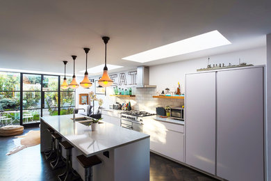 Large contemporary single-wall open plan kitchen in London with a double-bowl sink, flat-panel cabinets, grey cabinets, composite countertops, white splashback, ceramic splashback, stainless steel appliances, dark hardwood flooring, an island, brown floors and grey worktops.