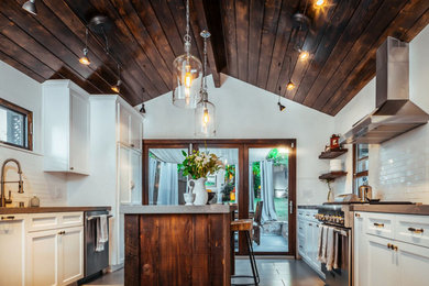 Photo of a large urban u-shaped kitchen/diner in Los Angeles with a double-bowl sink, recessed-panel cabinets, white cabinets, wood worktops, white splashback, metro tiled splashback, stainless steel appliances, an island, limestone flooring and brown floors.