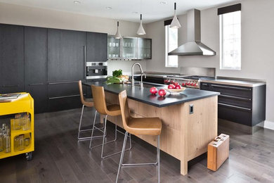 Large transitional l-shaped medium tone wood floor eat-in kitchen photo in Detroit with an undermount sink, flat-panel cabinets, black cabinets, quartz countertops, paneled appliances and an island