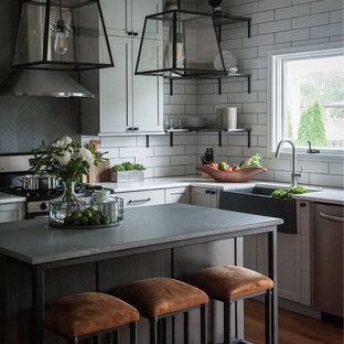 Diseño de cocina comedor en U, industrial, de tamaño medio, con fregadero sobremueble, armarios estilo shaker, puertas de armario grises, encimera de cuarzo compacto, salpicadero blanco, salpicadero de azulejos de cerámica, electrodomésticos de acero inoxidable, suelo de madera clara, una isla, suelo beige y encimeras grises