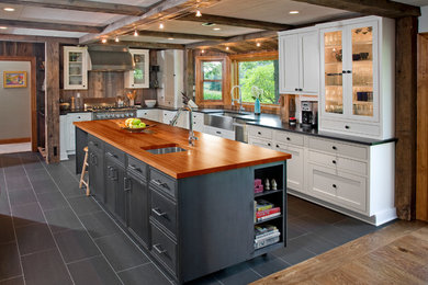 Industrial l-shaped kitchen in Philadelphia with a belfast sink, glass-front cabinets, white cabinets, wood worktops, brown splashback, wood splashback, stainless steel appliances, an island and grey floors.