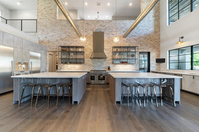 Inspiration for a large industrial u-shaped painted wood floor and brown floor open concept kitchen remodel in Houston with an undermount sink, flat-panel cabinets, distressed cabinets, quartz countertops, multicolored backsplash, stone tile backsplash, stainless steel appliances, two islands and gray countertops