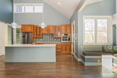 Example of a transitional medium tone wood floor kitchen design in Other with a farmhouse sink, quartz countertops, blue backsplash, cement tile backsplash, stainless steel appliances and an island