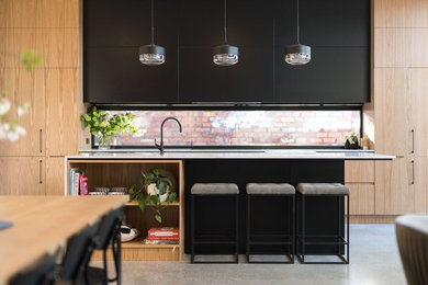 Idéer för funkis kök, med en nedsänkt diskho, luckor med infälld panel, svarta skåp, bänkskiva i kvarts, glaspanel som stänkskydd, svarta vitvaror, betonggolv och en köksö