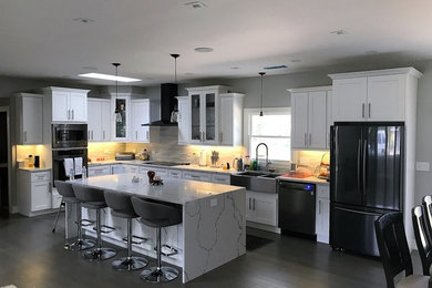 Example of a mid-sized minimalist l-shaped dark wood floor and brown floor eat-in kitchen design in Chicago with a farmhouse sink, shaker cabinets, white cabinets, quartz countertops, stainless steel appliances, an island and white countertops