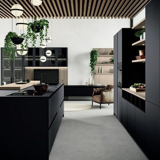 Immagine di una cucina minimalista di medie dimensioni con lavello da incasso, ante lisce, ante nere, top in legno, elettrodomestici neri, pavimento in cemento, isola, pavimento grigio e top marrone