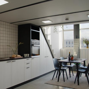 Design ideas for a medium sized modern single-wall open plan kitchen in London with a built-in sink, flat-panel cabinets, light wood cabinets, composite countertops, white splashback, ceramic splashback, black appliances, concrete flooring, no island, grey floors and black worktops.