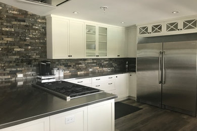 Photo of a small rustic l-shaped kitchen/diner in New York with grey splashback, brick splashback, stainless steel appliances and multiple islands.