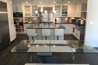 Inspiration for a mid-sized contemporary l-shaped kitchen remodel in Miami with a farmhouse sink, shaker cabinets, white cabinets, quartzite countertops, metallic backsplash, stainless steel appliances and an island