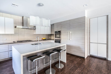 Photo of a medium sized modern u-shaped kitchen/diner in Los Angeles with a submerged sink, flat-panel cabinets, engineered stone countertops, white splashback, ceramic splashback, stainless steel appliances, medium hardwood flooring, an island, brown floors, white worktops and white cabinets.