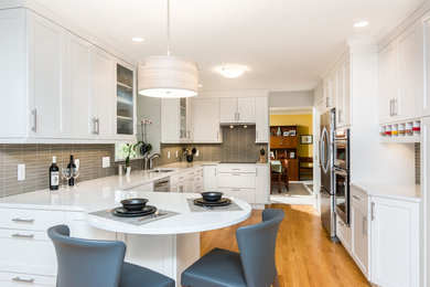 Large traditional galley open plan kitchen in Detroit with a submerged sink, recessed-panel cabinets, white cabinets, granite worktops, grey splashback, ceramic splashback, stainless steel appliances, light hardwood flooring and an island.