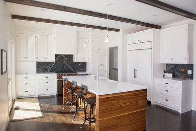 Transitional dark wood floor kitchen photo in New York with a farmhouse sink, shaker cabinets, white cabinets, gray backsplash, stainless steel appliances and an island