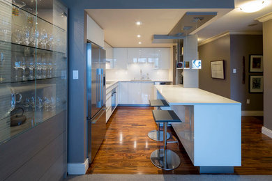 Example of a minimalist medium tone wood floor open concept kitchen design in Vancouver with glass-front cabinets, white cabinets, solid surface countertops and stainless steel appliances