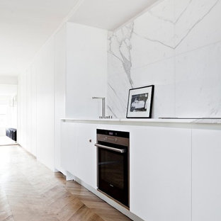 Idées déco pour une cuisine ouverte linéaire moderne de taille moyenne avec des portes de placard blanches, un plan de travail en marbre, une crédence blanche, un sol en bois brun, aucun îlot, un placard à porte plane, un électroménager noir et une crédence en marbre.