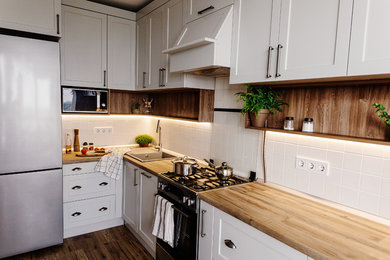 ワシントンD.C.にある高級な中くらいなトランジショナルスタイルのおしゃれなキッチン (ドロップインシンク、落し込みパネル扉のキャビネット、白いキャビネット、木材カウンター、白いキッチンパネル、セラミックタイルのキッチンパネル、シルバーの調理設備、濃色無垢フローリング、茶色い床、茶色いキッチンカウンター) の写真
