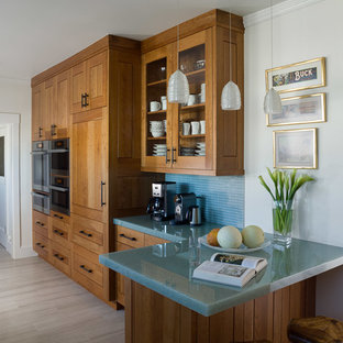 This is an example of a mid-sized contemporary galley separate kitchen in San Francisco with a double-bowl sink, shaker cabinets, medium wood cabinets, glass benchtops, blue splashback, matchstick tile splashback, stainless steel appliances, porcelain floors, a peninsula and turquoise benchtop.