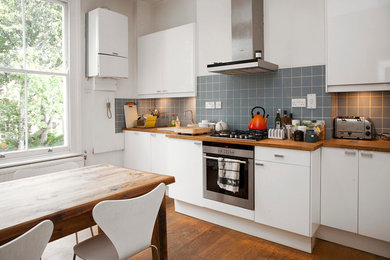 ロンドンにあるお手頃価格の中くらいなコンテンポラリースタイルのおしゃれなキッチン (エプロンフロントシンク、フラットパネル扉のキャビネット、白いキャビネット、木材カウンター、青いキッチンパネル、セラミックタイルのキッチンパネル、シルバーの調理設備、無垢フローリング、アイランドなし) の写真