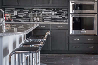 Example of a large minimalist galley ceramic tile open concept kitchen design in Jacksonville with a farmhouse sink, flat-panel cabinets, black cabinets, granite countertops, multicolored backsplash, ceramic backsplash, stainless steel appliances and an island