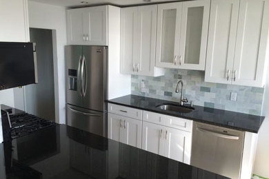 Example of a mid-sized minimalist galley medium tone wood floor enclosed kitchen design in New York with an undermount sink, shaker cabinets, white cabinets, quartz countertops, blue backsplash, subway tile backsplash, stainless steel appliances and no island