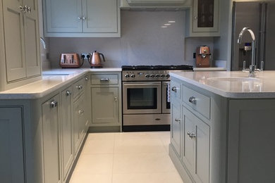 Large traditional l-shaped kitchen/diner in Other with a built-in sink, shaker cabinets, green cabinets, quartz worktops, white splashback, stainless steel appliances, porcelain flooring, an island, white floors and white worktops.