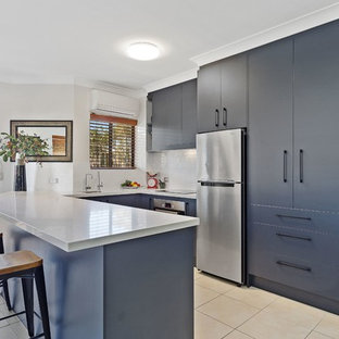This is an example of a contemporary u-shaped kitchen in Gold Coast - Tweed with an undermount sink, flat-panel cabinets, blue cabinets, white splashback, stone tile splashback, stainless steel appliances and a peninsula.