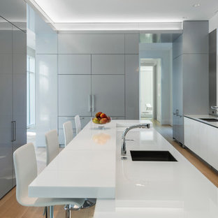 Diseño de cocina moderna con fregadero de doble seno, armarios con paneles lisos, puertas de armario blancas, salpicadero verde, salpicadero de vidrio templado, suelo de madera clara y una isla