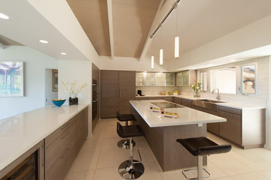 This is an example of a medium sized contemporary u-shaped kitchen/diner in Hawaii with a belfast sink, flat-panel cabinets, dark wood cabinets, quartz worktops, white splashback, glass tiled splashback, stainless steel appliances, ceramic flooring, an island and beige floors.
