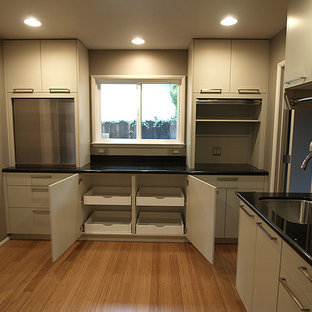 Small modern l-shaped kitchen pantry in Sacramento with an undermount sink, flat-panel cabinets, beige cabinets, granite benchtops, beige splashback, glass tile splashback, stainless steel appliances, bamboo floors and no island.