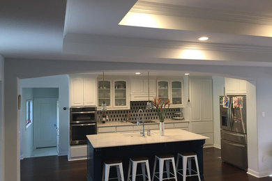 Example of a minimalist dark wood floor kitchen design in Dallas with a double-bowl sink, raised-panel cabinets, white cabinets, quartz countertops, multicolored backsplash, porcelain backsplash, stainless steel appliances and an island