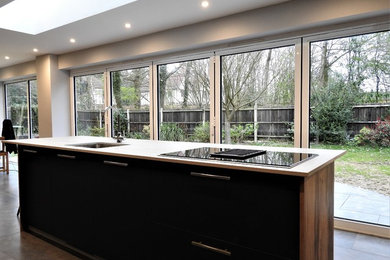 Inspiration for a medium sized modern l-shaped kitchen/diner in Kent with a submerged sink, flat-panel cabinets, black cabinets, black appliances, an island and white worktops.