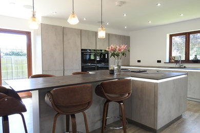 This is an example of a medium sized contemporary l-shaped enclosed kitchen in Other with a submerged sink, flat-panel cabinets, grey cabinets, black appliances, an island, brown floors and multicoloured worktops.