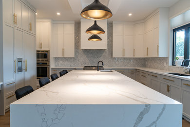 Example of a large trendy u-shaped plywood floor and yellow floor eat-in kitchen design in Toronto with a drop-in sink, shaker cabinets, quartz countertops, gray backsplash, ceramic backsplash, stainless steel appliances, an island and white countertops