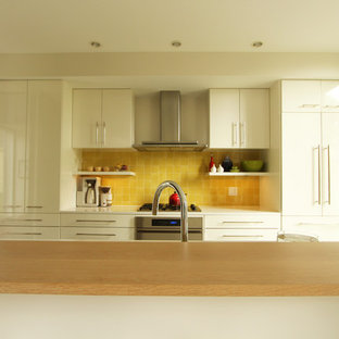Photo of a small modern single-wall open plan kitchen in Other with a double-bowl sink, flat-panel cabinets, white cabinets, quartz benchtops, yellow splashback, ceramic splashback, panelled appliances, concrete floors and with island.