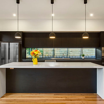 Modern kitchen with stone island bench, feature lighting and glass splash back
