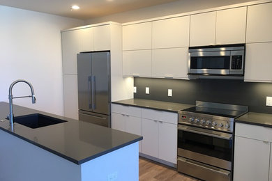 Mid-sized minimalist galley medium tone wood floor and brown floor eat-in kitchen photo in Denver with a single-bowl sink, flat-panel cabinets, white cabinets, solid surface countertops, white backsplash, stone slab backsplash, stainless steel appliances and no island