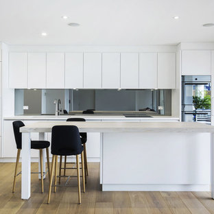 Inspiration for a contemporary single-wall kitchen in Sydney with an undermount sink, flat-panel cabinets, white cabinets, glass sheet splashback, light hardwood floors, with island, brown floor and grey benchtop.