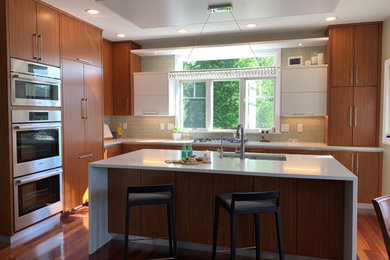Trendy l-shaped medium tone wood floor and brown floor kitchen photo in Other with a double-bowl sink, flat-panel cabinets, medium tone wood cabinets, quartzite countertops, gray backsplash, glass tile backsplash, paneled appliances, an island and white countertops