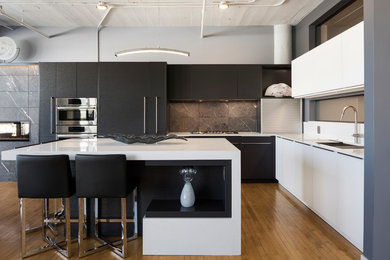 Moderne Küche in L-Form mit Unterbauwaschbecken, flächenbündigen Schrankfronten, schwarzen Schränken, Küchenrückwand in Grau, Elektrogeräten mit Frontblende, braunem Holzboden, Kücheninsel, braunem Boden und weißer Arbeitsplatte in Minneapolis
