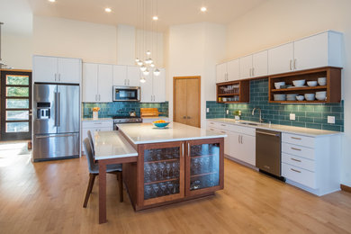 Open concept kitchen - large contemporary l-shaped light wood floor open concept kitchen idea in Portland with an undermount sink, flat-panel cabinets, white cabinets, quartz countertops, blue backsplash, glass tile backsplash, stainless steel appliances, an island and white countertops