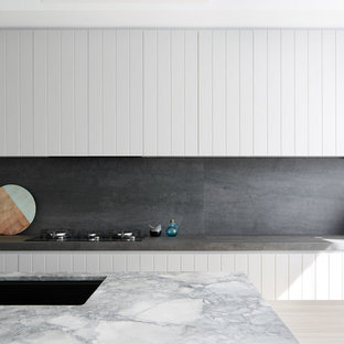 Contemporary galley kitchen in Sydney with an undermount sink, white cabinets, grey splashback, stone slab splashback, with island and grey benchtop.
