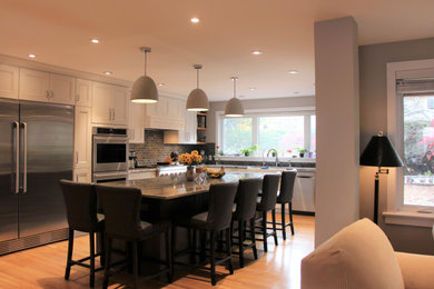 Example of a large trendy l-shaped medium tone wood floor kitchen design in Ottawa with a farmhouse sink, recessed-panel cabinets, white cabinets, granite countertops, gray backsplash, brick backsplash, stainless steel appliances, an island and blue countertops