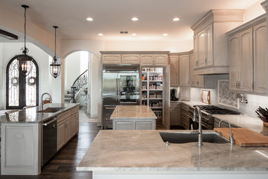 Inspiration for a large mediterranean u-shaped dark wood floor and brown floor kitchen pantry remodel in Austin with an undermount sink, raised-panel cabinets, gray cabinets, granite countertops, gray backsplash, mosaic tile backsplash, stainless steel appliances, two islands and gray countertops