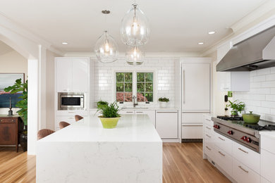 Large trendy l-shaped light wood floor eat-in kitchen photo in Portland with an undermount sink, flat-panel cabinets, white cabinets, quartz countertops, white backsplash, subway tile backsplash, stainless steel appliances and an island