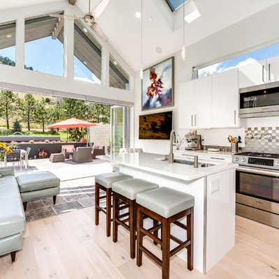 Example of a small trendy l-shaped light wood floor open concept kitchen design in Denver with a double-bowl sink, flat-panel cabinets, white cabinets, solid surface countertops, gray backsplash, metal backsplash, stainless steel appliances and an island