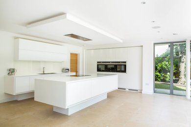 Inspiration for a medium sized contemporary galley open plan kitchen in Wiltshire with an integrated sink, flat-panel cabinets, white cabinets, composite countertops, white splashback, glass sheet splashback, black appliances, limestone flooring, an island, beige floors and white worktops.