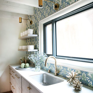 Modelo de cocina moderna con fregadero bajoencimera, armarios con paneles lisos, puertas de armario blancas, encimera de cuarcita, salpicadero azul, salpicadero de azulejos de cemento, electrodomésticos de acero inoxidable y suelo de ladrillo