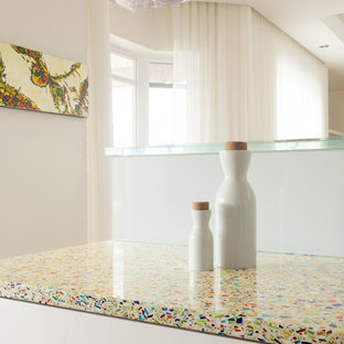 Exemple d'une cuisine parallèle moderne fermée et de taille moyenne avec un évier encastré, un placard à porte plane, des portes de placard blanches, un plan de travail en verre recyclé, une crédence blanche, une crédence en feuille de verre, un électroménager blanc, un sol en bois clair et aucun îlot.