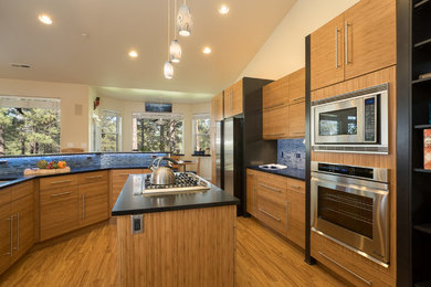 Example of a mid-sized trendy medium tone wood floor and brown floor kitchen design in Phoenix with an undermount sink, flat-panel cabinets, medium tone wood cabinets, granite countertops, blue backsplash, matchstick tile backsplash, stainless steel appliances and an island